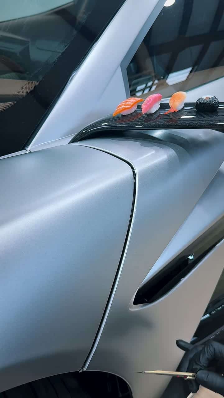 Rolling a film edge into the fender gap of a satin-silver Aston Martin Valhalla, sushi on the fender