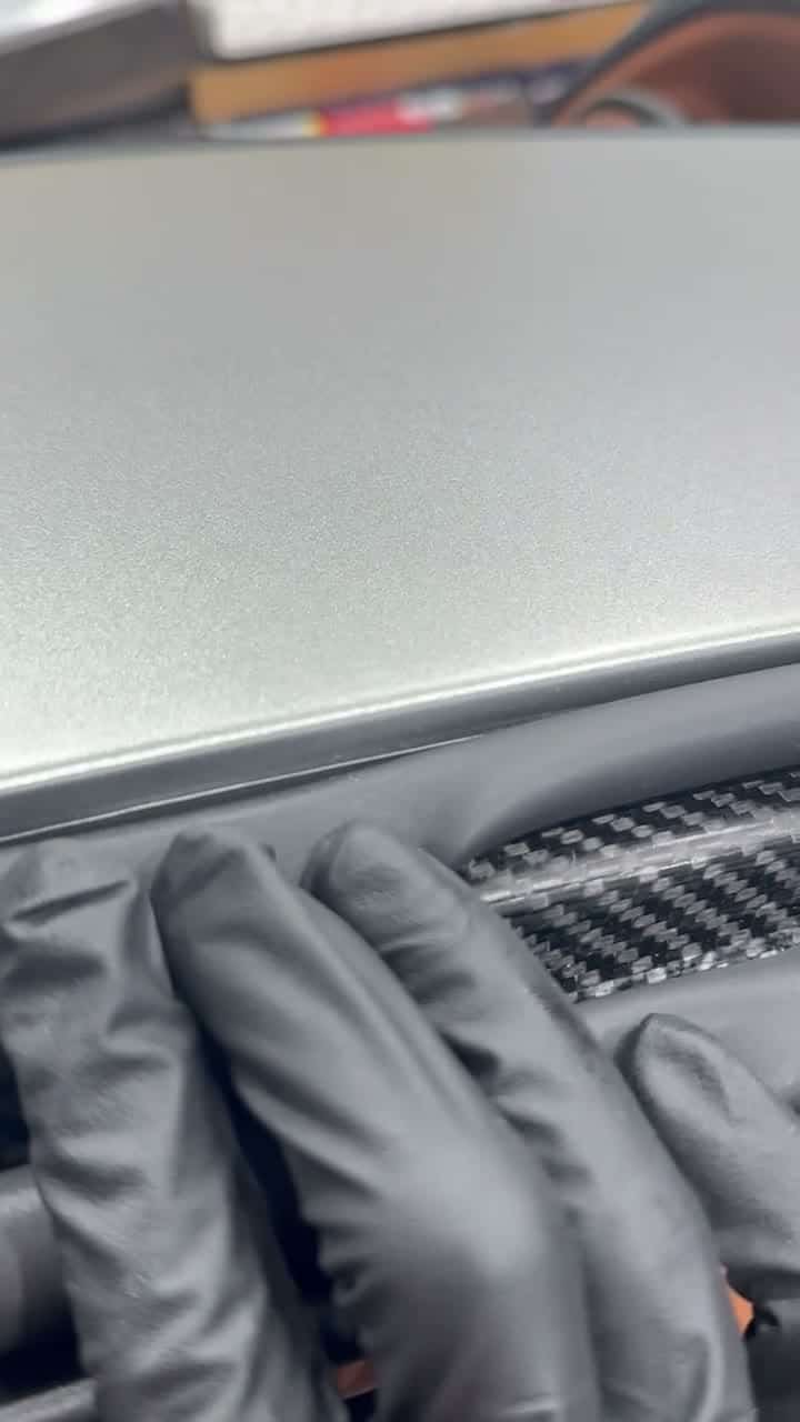 Film edge tucked under the rubber seal beside a carbon fiber trim strip