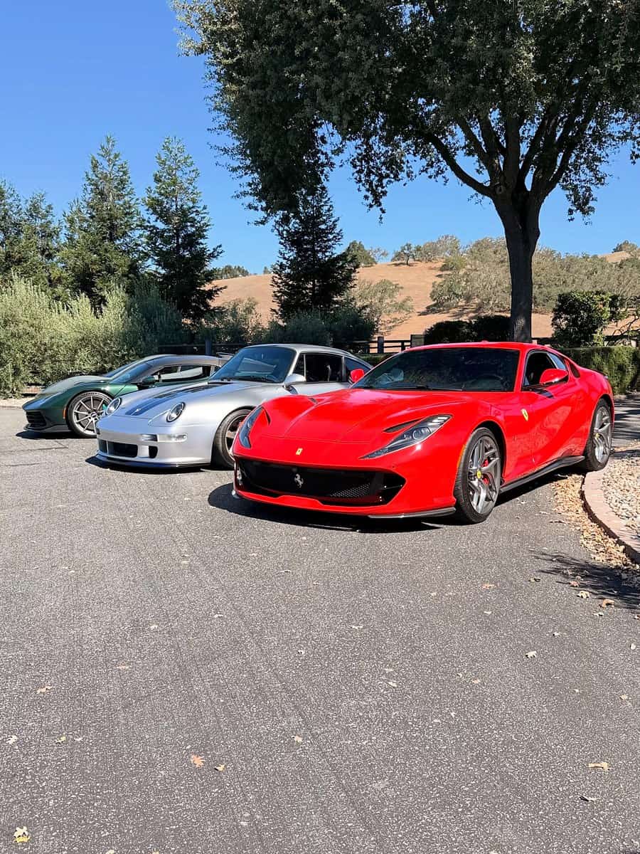 Ferrari 812 and other cars lined up under trees