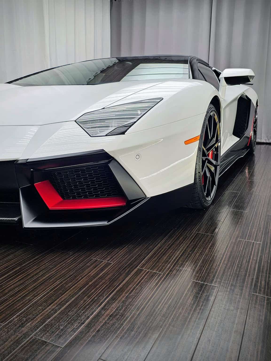 White Lamborghini Aventador with red front intake accents in the shop's photo bay